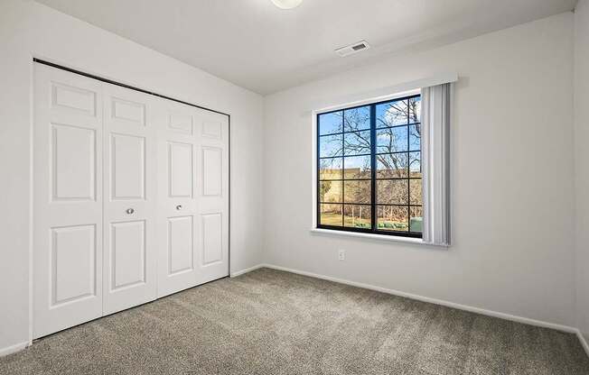 A bedroom with a large window and a white closet at Tanglewood Apartments, Oak Creek, WI