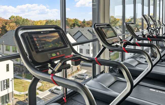 a row of cardio machines in a gym overlooking a window