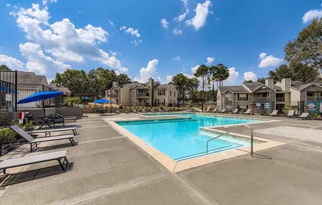 A swimming pool surrounded by sun loungers and apartment buildings.