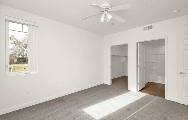 an empty bedroom with a ceiling fan and a door to a bathroom