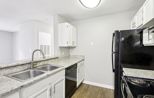 A kitchen with a black refrigerator, white cabinets, and a granite countertop.