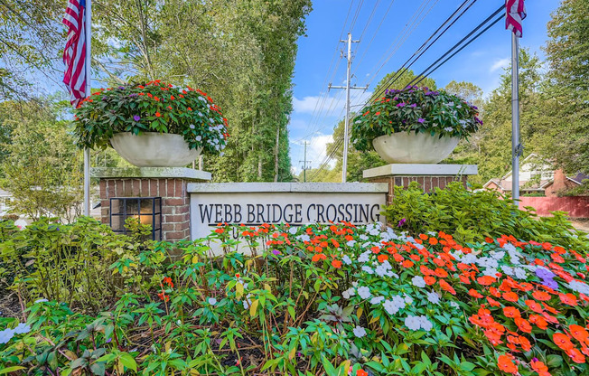 A sign that says Webb Bridge Crossing is surrounded by flowers.