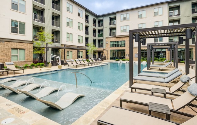 a swimming pool with lounge chairs in front of an apartment building