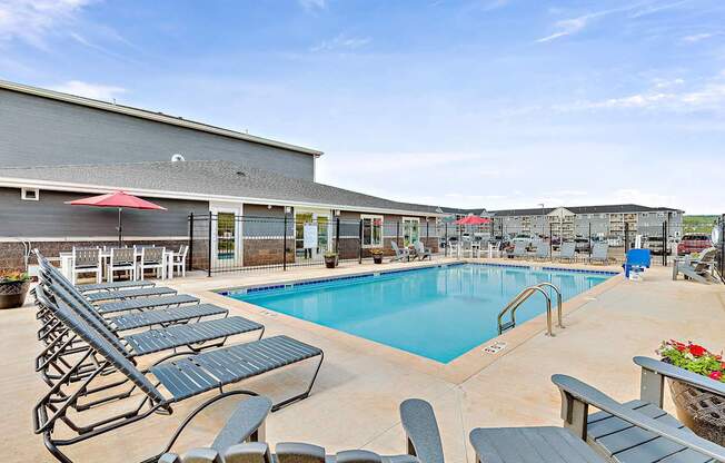 A pool with lounge chairs and umbrellas in front of a building.