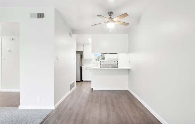 A room with a ceiling fan and a kitchen island in the background.