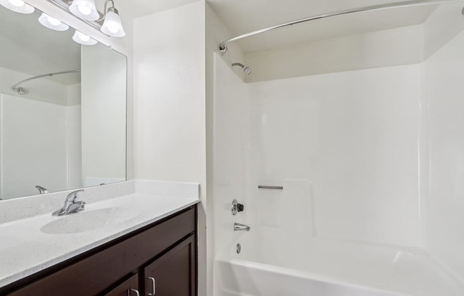 A white bathroom with a sink, mirror, and bathtub.