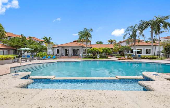 A large swimming pool surrounded by a concrete patio and palm trees.