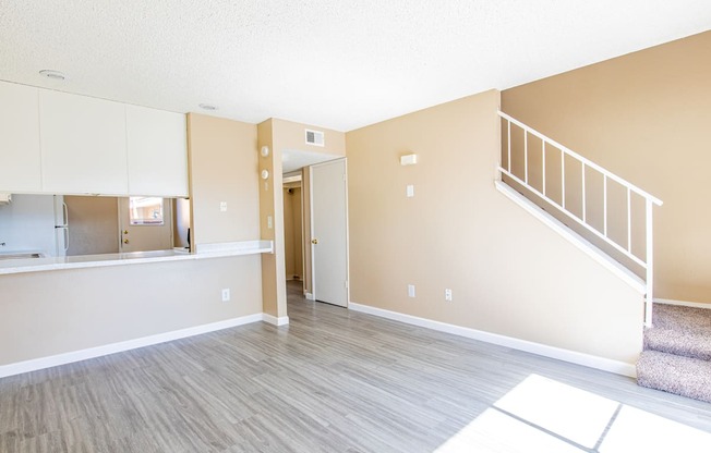 an empty living room with a staircase and a kitchen