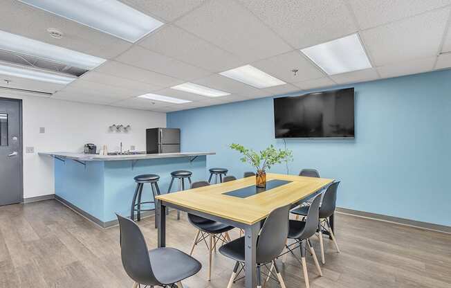 a conference room with a table and chairs with a kitchenette in the background