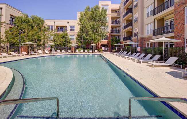 A large swimming pool surrounded by sun loungers and apartment buildings.