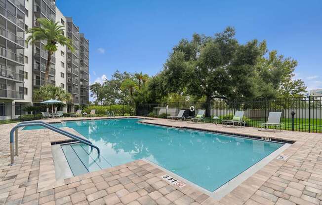 A swimming pool surrounded by a brick patio and lounge chairs at Hampton Apartments, Clearwater, FL, 33759