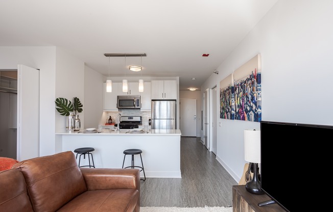 A brown leather couch is in the foreground of a modern kitchen and living room.