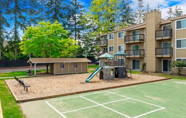 A playground with a slide and a basketball court in front of apartment buildings.