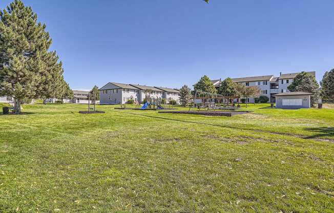 a large grassy area with a playground and houses in the background