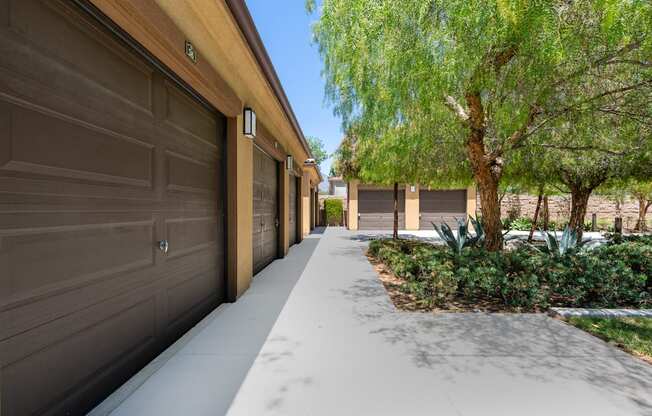 A long driveway with a row of garage doors on one side and a tree on the other.