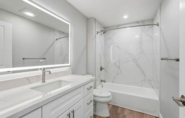 A white bathroom with a marble shower and a white toilet.