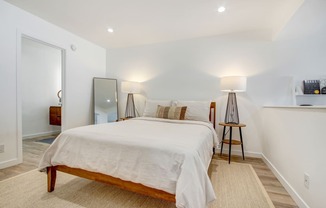 Sleeping area with recessed lights, plank flooring, bathroom on the left