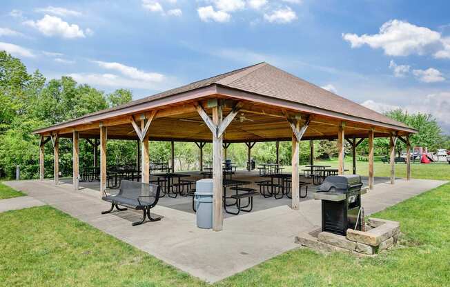 A pavilion with a brown roof and wooden pillars is surrounded by a grassy area with picnic tables and trash cans at Hummingbird Pointe & The Gardens, Parma, Ohio