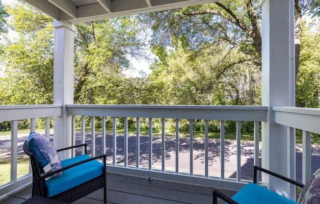 a porch with two chairs and a view of the street and trees