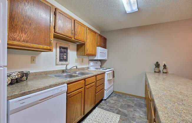 a kitchen with a sink and dishwasher and wooden cabinets. Fargo, ND Kennedy Apartments