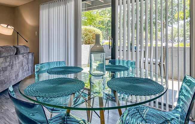 A glass table with four chairs in front of a window with blinds.