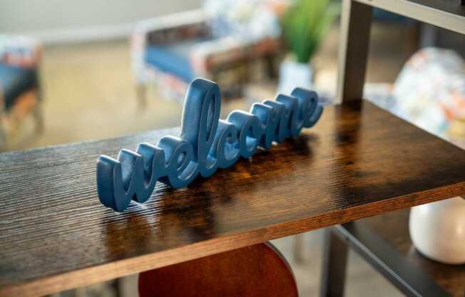 A blue 3D printed word "welcome" on a wooden surface.