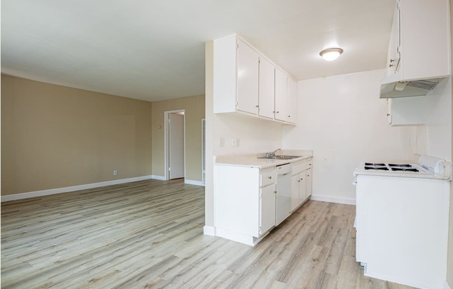 an empty kitchen and living room with white cabinets and wood floors