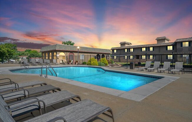 A pool surrounded by lounge chairs and a building in the background.