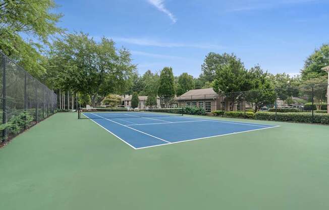 A tennis court surrounded by trees and a fence.