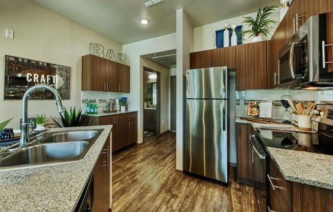 The Craft at Gilbert and Baseline. Apartment kitchen with stainless steel double sink and stainless steel refrigerator.  Beautiful modern cabinets line kitchen walls and surround black range.