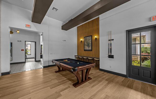 A pool table is in the middle of a room with a door to the left and a window to the right.