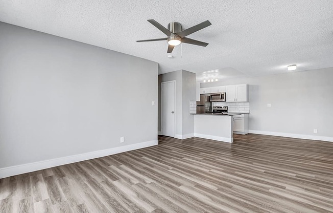 a living room with a ceiling fan and a kitchen in the background