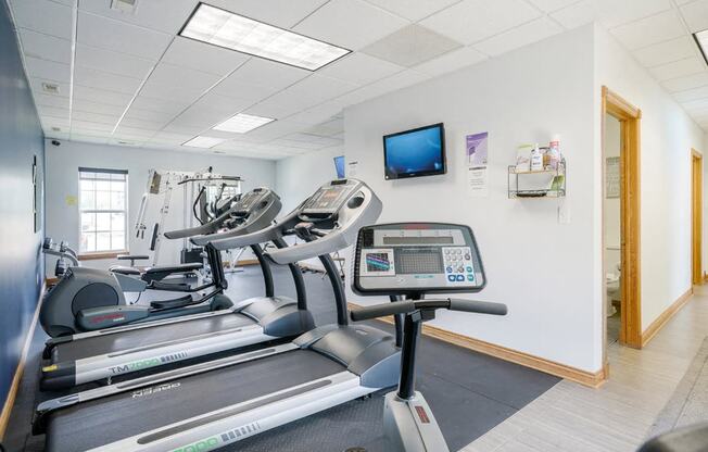 24-hour fitness center with a stationary bike, two treadmills, and an elliptical with a tv on the wall