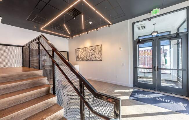 A staircase with a metal railing leads to a brightly lit room with a large painting on the wall.
