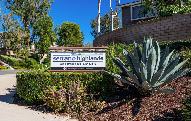 a sign for serrano highlands apartments in front of a plant