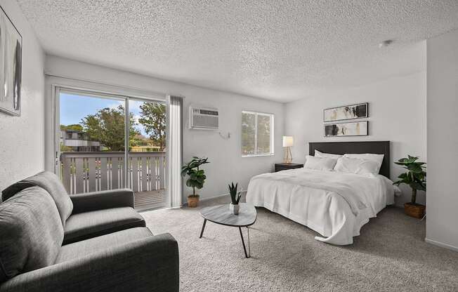 A bedroom with a large bed, grey couch, and a small table.