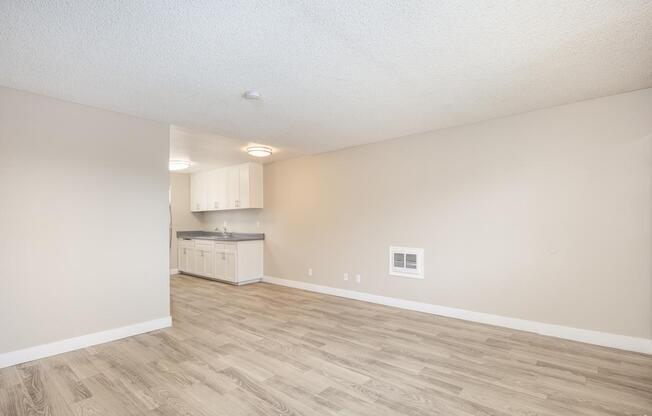 A room with a kitchenette in the background and a hardwood floor.