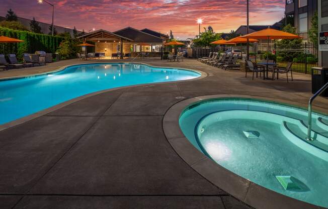 a swimming pool at dusk with umbrellas and a building in the background