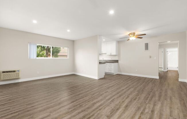 an empty living room with a kitchen in the background