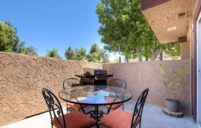 a patio with a glass table and chairs and a grill