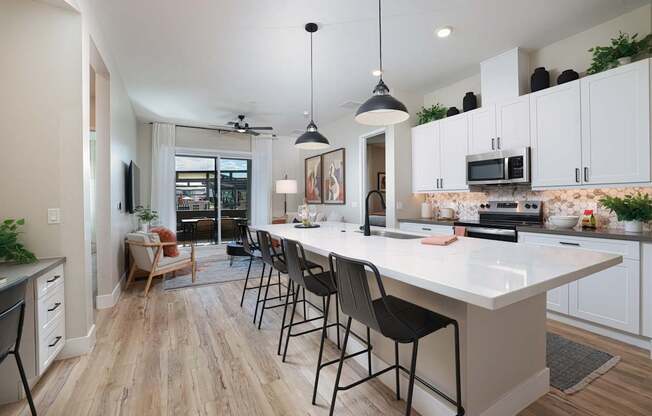 A modern kitchen with a white island and black chairs.