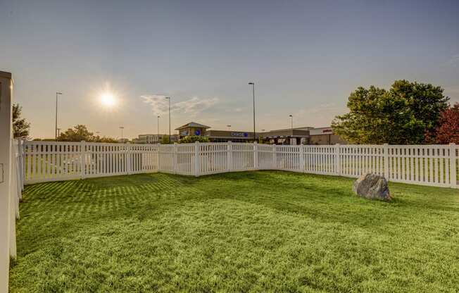 a yard with a white fence and a rock in the grass