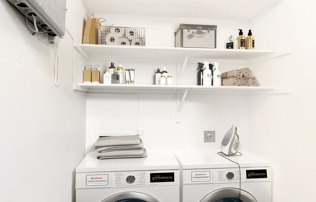 Virtually staged laundry area with washer, dryer, clothes iron, and products on shelves above