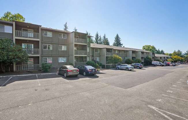 A parking lot in front of apartment buildings with cars parked.
