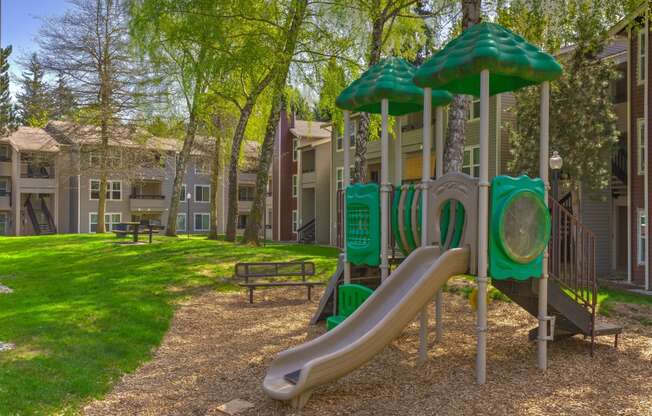 a playground with a slide and umbrella in front of an apartment building