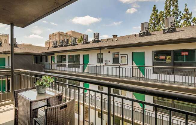 A balcony with a table and chairs overlooks a building with green and white doors.
