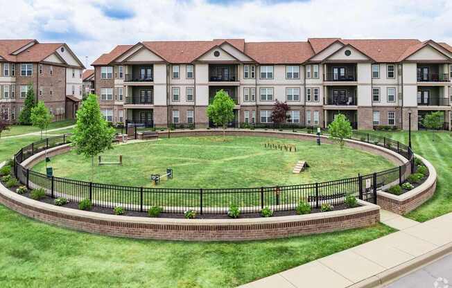 A large grassy area surrounded by a black fence in front of apartment buildings.