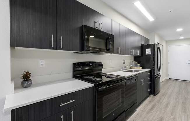 a kitchen with dark cabinets, white countertops, efficient appliances, and plank flooring at Arabella Apartment Homes, Washington, 98155