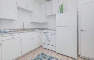 A white kitchen with a refrigerator, sink, and cabinets.