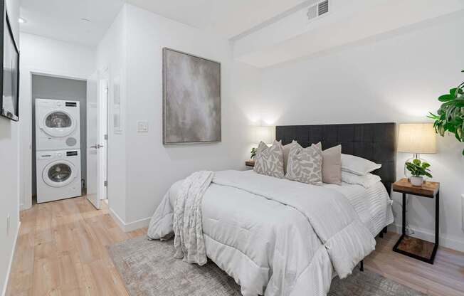 A bedroom with a large bed and a washing machine in the corner.